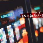 Eine Nahaufnahme von beleuchteten Spielautomaten in einem Kasino mit dem deutschen Wort sensibilisieren in Schreibschrift quer über das Bild geschrieben.