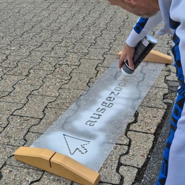 Der Einrichtungsleiter Beratung & Behandlung, René Fischer, sprüht mit Kreidefarbe und einer Schablone den Schriftzug abgezockt.de auf den Boden.