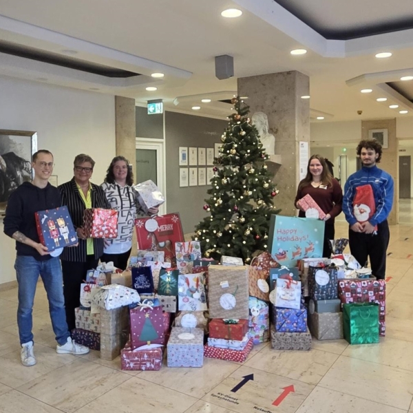 Die Organisatorinnen des Luisenhospitals übergeben vor dem Wunschbaum die vielen Geschenke an Mitarbeitende der Suchthilfe Aachen.