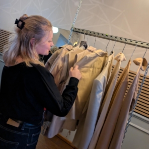 Eine Frau stöbert durch sortierte Kleidung, die an einer Kleiderstange hängen.