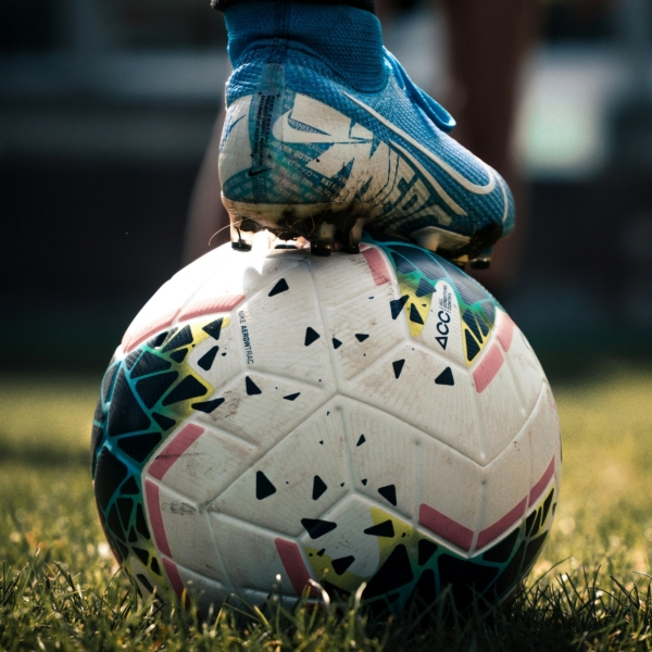 Ein Fußball liegt auf dem Rasen, darauf steht ein Fuß in Fußballschuhen.
